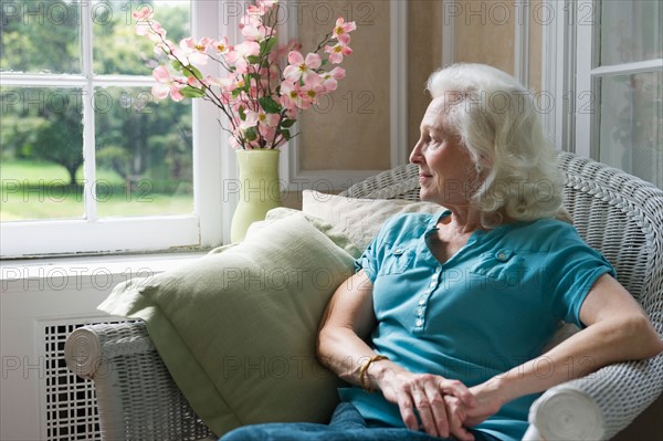 Senior woman sitting in chair looking through window.