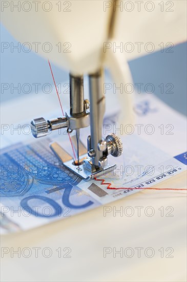 Sewing machine stitching 20 euro note, studio shot.