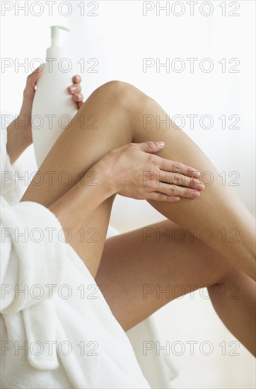 Midsection of woman applying skin moisturizer, studio shot.