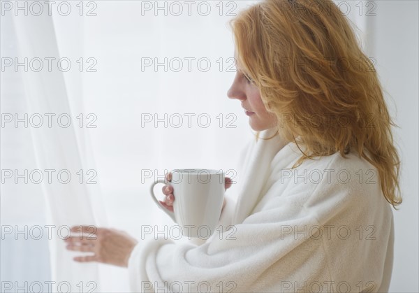 Woman in bathrobe looking out window.