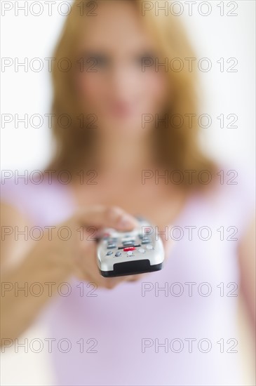 Woman holding remote control, focus on foreground, studio shot.