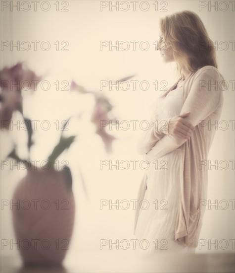 Woman standing behind vase, studio shot.