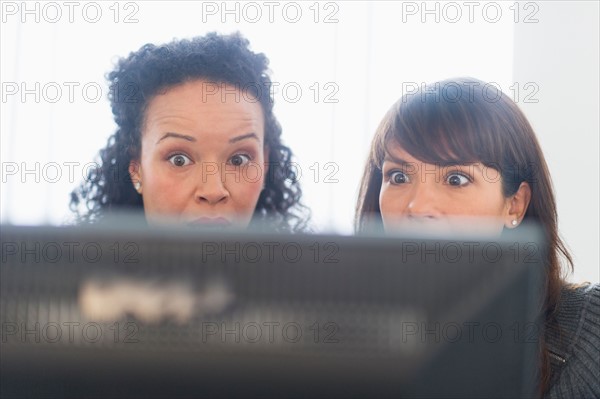 Two business women behind computer looking frightened.