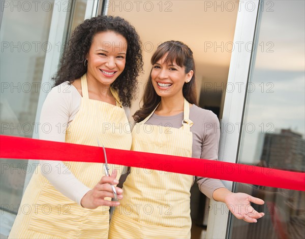 Two female business owners cutting red ribbon.