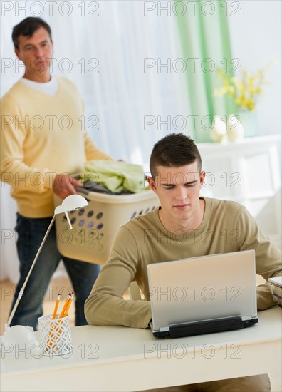 Son (16-17) using laptop being observed by father.