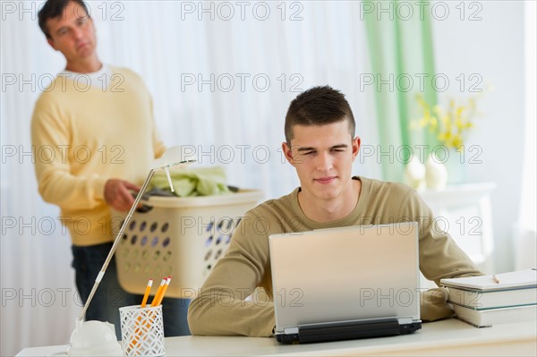 Son (16-17) using laptop being observed by father.