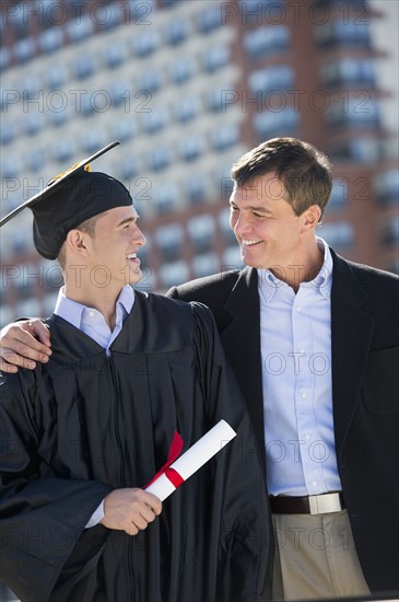 Father with teenage sun (16-17) at graduation ceremony.