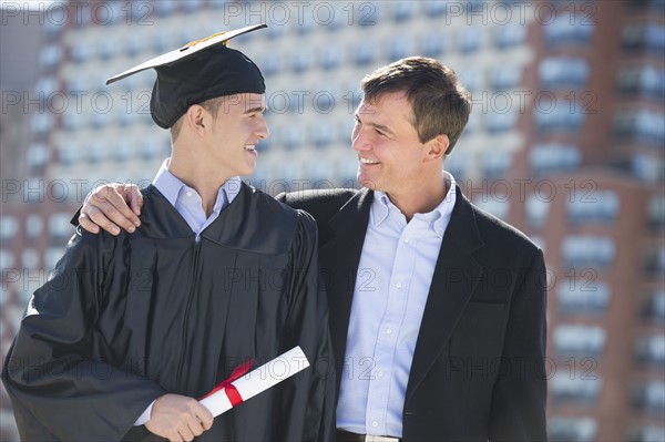 Father with teenage sun (16-17) at graduation ceremony.