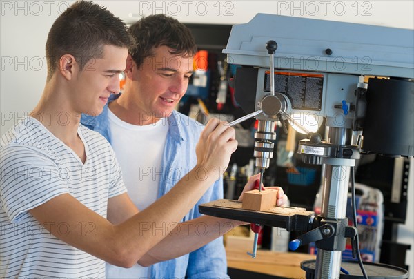 Man with teenage son (16-17) drilling in workshop.
