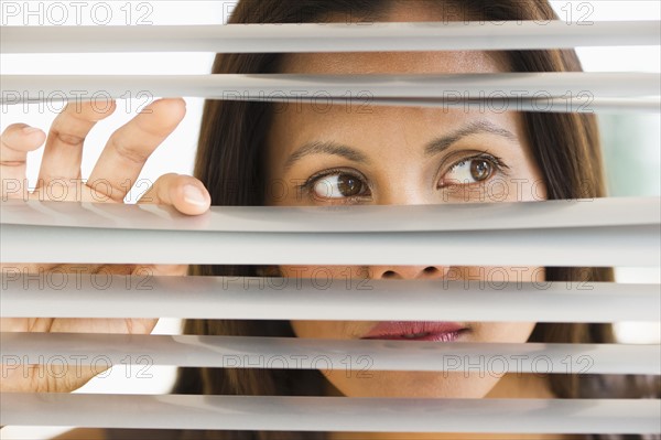 Studio shot of woman looking through blinds.