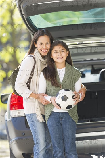 Portrait of mother with daughter (10-11) holding soccer ball.