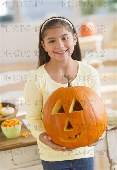 Portrait of girl (10-11) holding Jack o lantern.