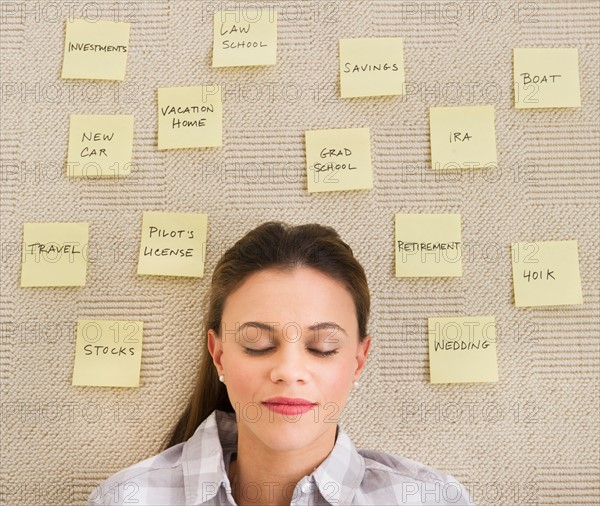 Woman lying on carpet with adhesive notes around head.