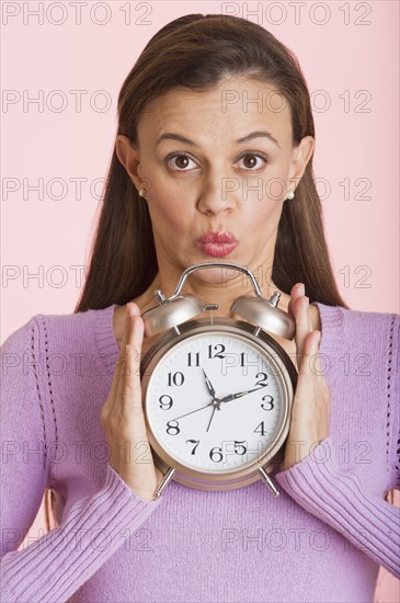 Studio shot of woman holding alarm clock.