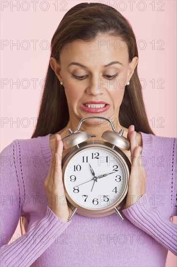 Studio shot of woman holding alarm clock.