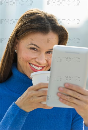 Woman working on digital tablet and drinking coffee.