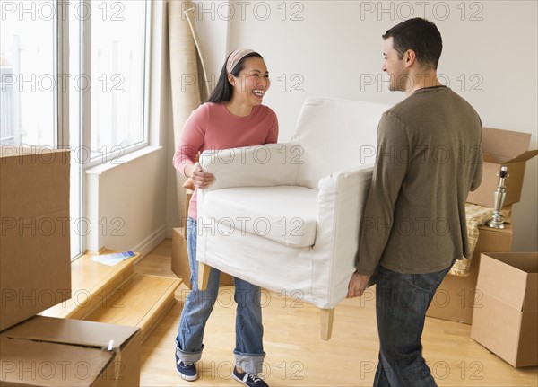 Man and woman carrying chair in new house.