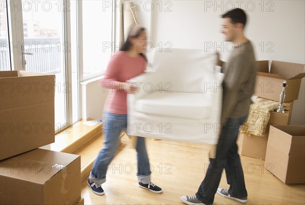 Man and woman carrying chair in new house.