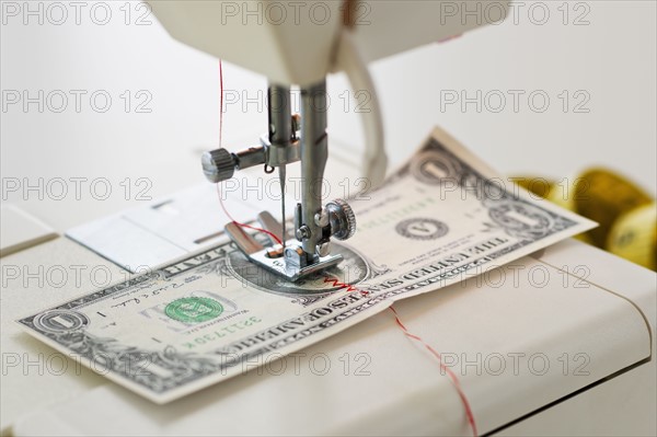 Halves of dollar bill being sewed with sewing machine.