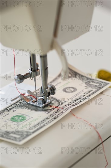 Halves of dollar bill being sewed with sewing machine.