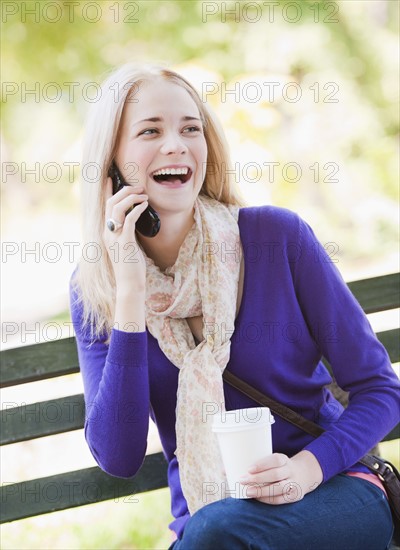 USA, New York, New York City, Manhattan, Central Park, Young woman sitting on bench and talking on mobile phone. Photo: Daniel Grill