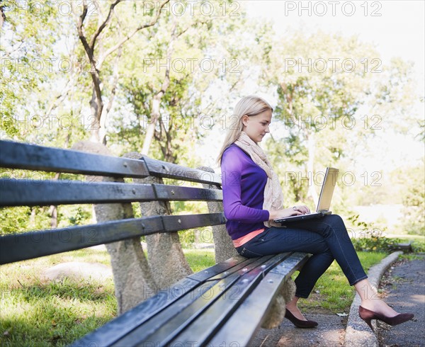 USA, New York, New York City, Manhattan, Central Park, Young woman sitting on bench and using laptop. Photo : Daniel Grill