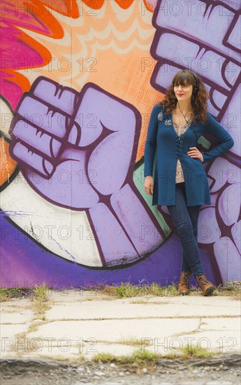 Woman standing against wall with graffiti. Photo : Daniel Grill