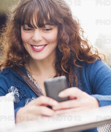 Woman sitting in sidewalk cafe and texting on mobile phone. Photo: Daniel Grill