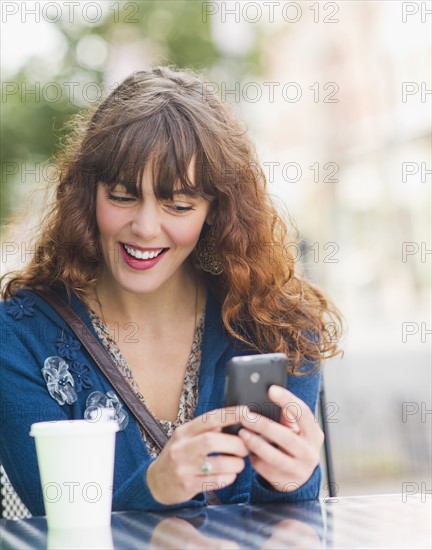 Woman sitting in sidewalk cafe and texting on mobile phone. Photo: Daniel Grill