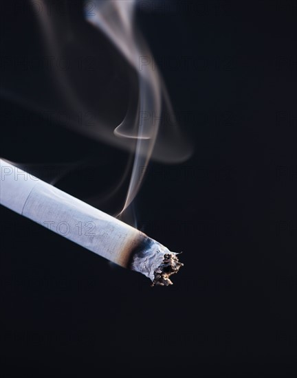 Close up of burning cigarette on black background. Photo : Daniel Grill