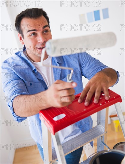 Man standing on ladder with paint roller. Photo : Daniel Grill