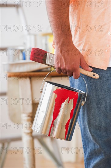 Close up of man's hand holding pain brush and paint can. Photo: Daniel Grill