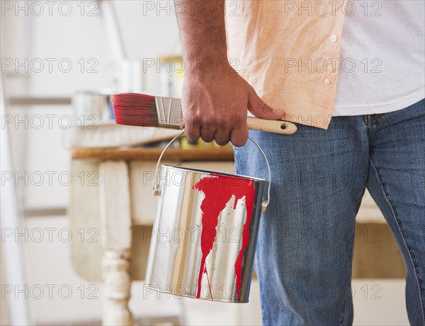 Close up of man's hand holding pain brush and paint can. Photo : Daniel Grill