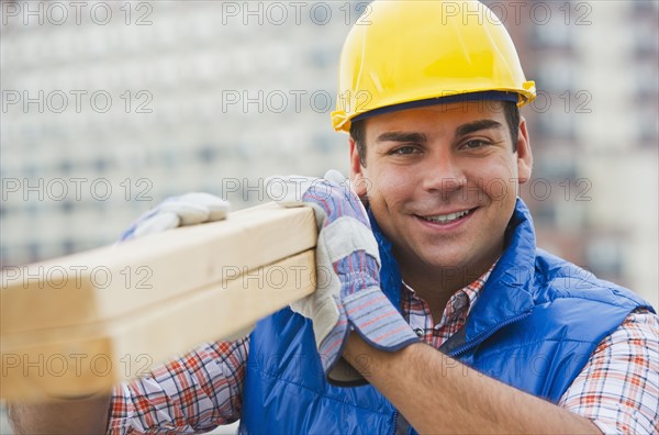 Construction worker carrying planks on construction site. Photo : Daniel Grill