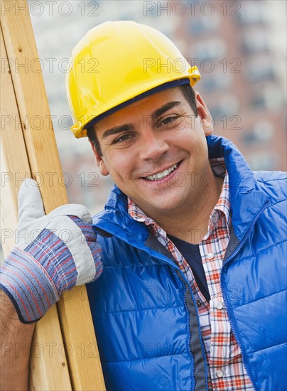 Construction worker carrying planks on construction site. Photo : Daniel Grill