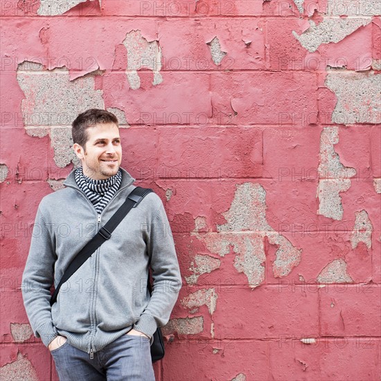 Man standing at front of old peeling red wall. Photo : Daniel Grill