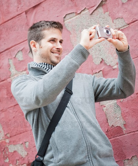 Man standing at front of old peeling red wall and photographing. Photo: Daniel Grill