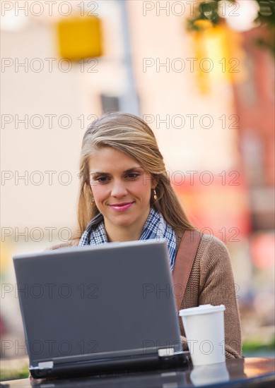 Young woman sitting with laptop in sidewalk cafe. Photo: Daniel Grill