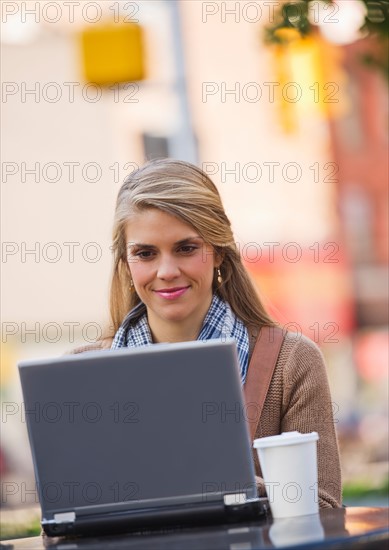 Young woman sitting with laptop in sidewalk cafe. Photo : Daniel Grill