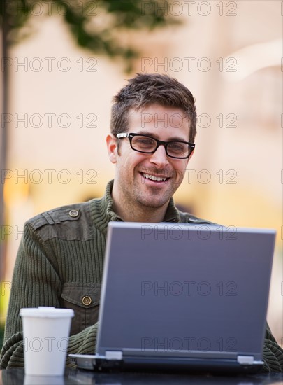 Young woman sitting with laptop in sidewalk cafe. Photo : Daniel Grill