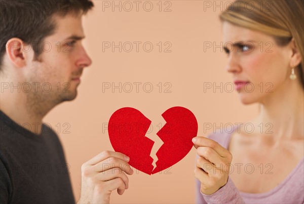 Couple holding red broken paper heart. Photo : Daniel Grill