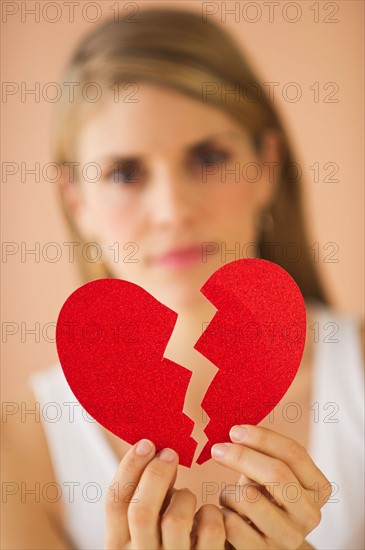Young woman holding broken paper heart. Photo : Daniel Grill