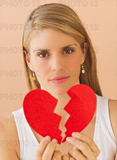 Young woman holding broken paper heart. Photo : Daniel Grill