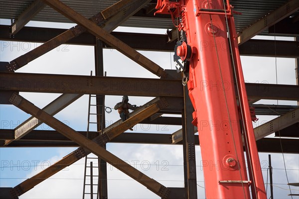 Construction worker working on unfinished structure, red crane in foreground. Photo : fotog