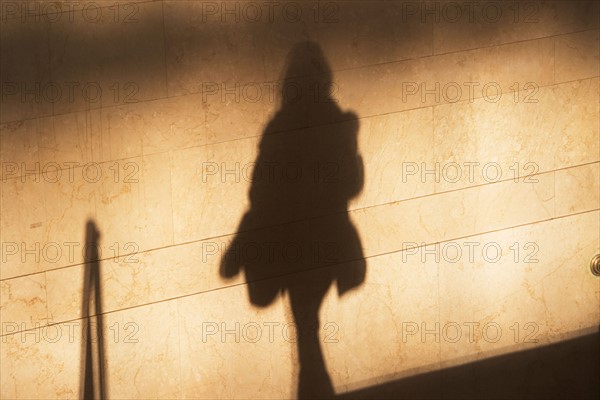 Shadow of female pedestrian on sunlit wall. Photo : fotog