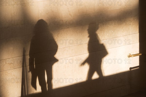 Shadow of two female pedestrians on sunlit wall. Photo : fotog