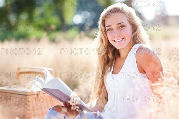 Teenage girl (16-17) posing for portrait while reading book outdoors. Photo : Take A Pix Media