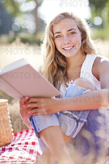 Teenage girl (16-17) posing for portrait while reading book outdoors. Photo : Take A Pix Media