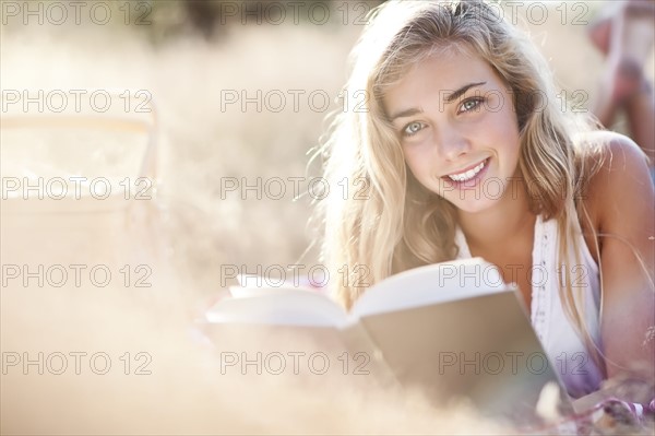 Teenage girl (16-17) posing for portrait while reading book outdoors. Photo : Take A Pix Media