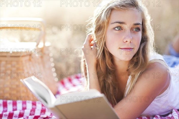 Teenage girl (16-17) taking break from reading book outdoors. Photo : Take A Pix Media